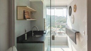 Un baño moderno con mampara de vidrio, encimera negra y vistas a la ciudad a través de un ventanal grande.
