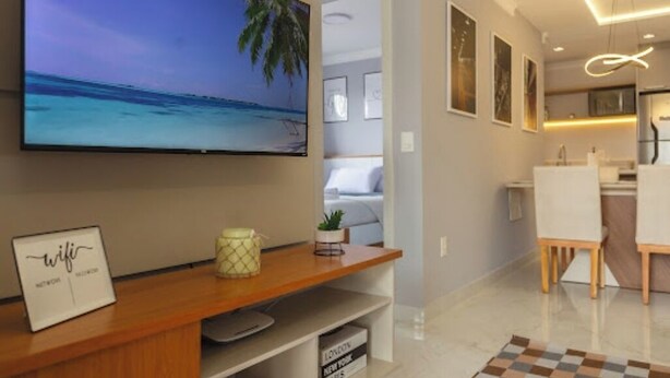 Una sala de estar moderna con un televisor de pantalla plana montado en la pared, un mueble de madera para entretenimiento, una alfombra a cuadros y un comedor con mesa y sillas.