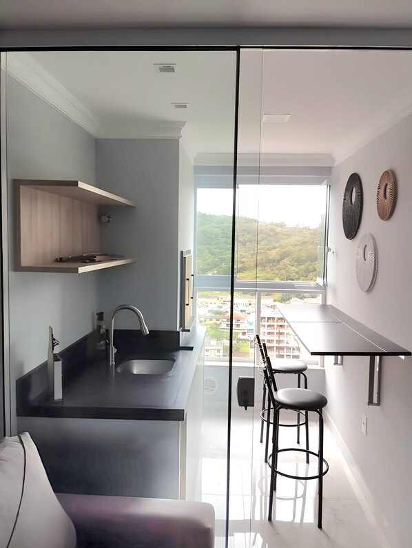A modern kitchen with a large island, a dining area with a table and chairs, and a view of a cityscape through large windows.