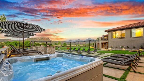 A hot tub, lounge chairs, and umbrellas in a backyard setting.