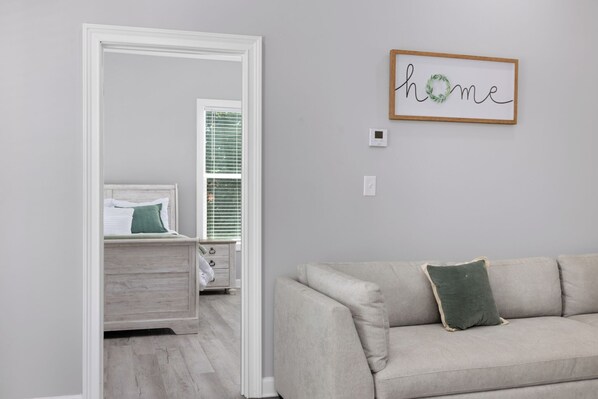 A room with a light-colored sofa, a bed with green bedding, and a wall-mounted sign that reads "home".