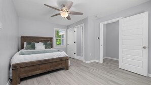 Une chambre à coucher avec un lit en bois, des murs blancs et un ventilateur de plafond.