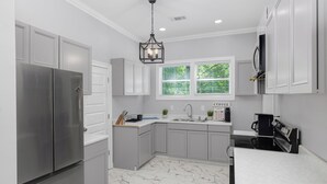 Une cuisine moderne avec des meubles gris, un réfrigérateur en acier inoxydable, un évier et un coin café.