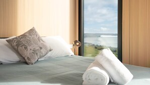 Una habitación de hotel con una cama, un ventanal con vistas al paisaje y una toalla enrollada sobre la cama.