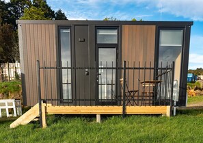 Una cabaña moderna y compacta, con terraza de madera, ventanas amplias y cercado de metal.