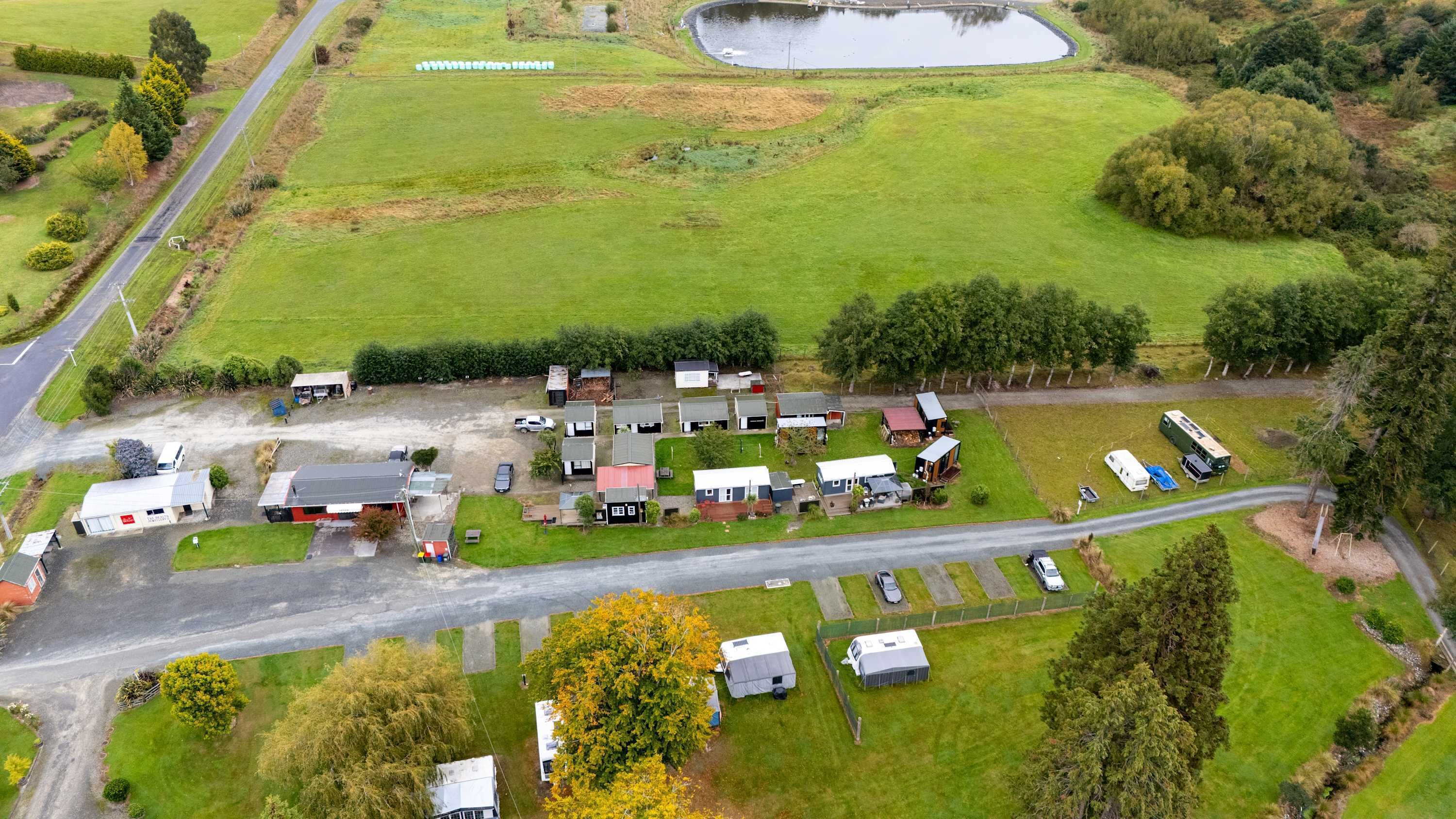 Vue aérienne d’une zone rurale avec un petit groupe de maisons, une route et un étang.