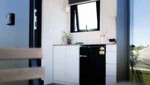 Een kleine keuken met witte kastjes, een zwarte koelkast, een raam en een potplant.