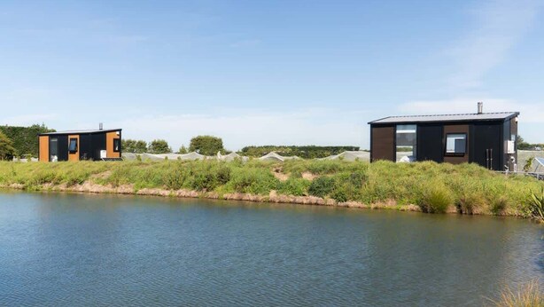 Twee moderne, minimalistische huizen aan een rustige rivier, omgeven door groen.