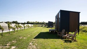 A modern outdoor seating area with a table and chairs, a small building, and rows of grapevines. - Vintners Retreat by Tiny Away (Burnham)