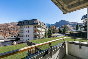 Un edificio de varios pisos con balcones, techo verde y vistas a las montañas.