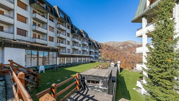 Un hôtel à plusieurs étages doté de balcons, d’une cour verdoyante et surplombant un paysage montagneux.