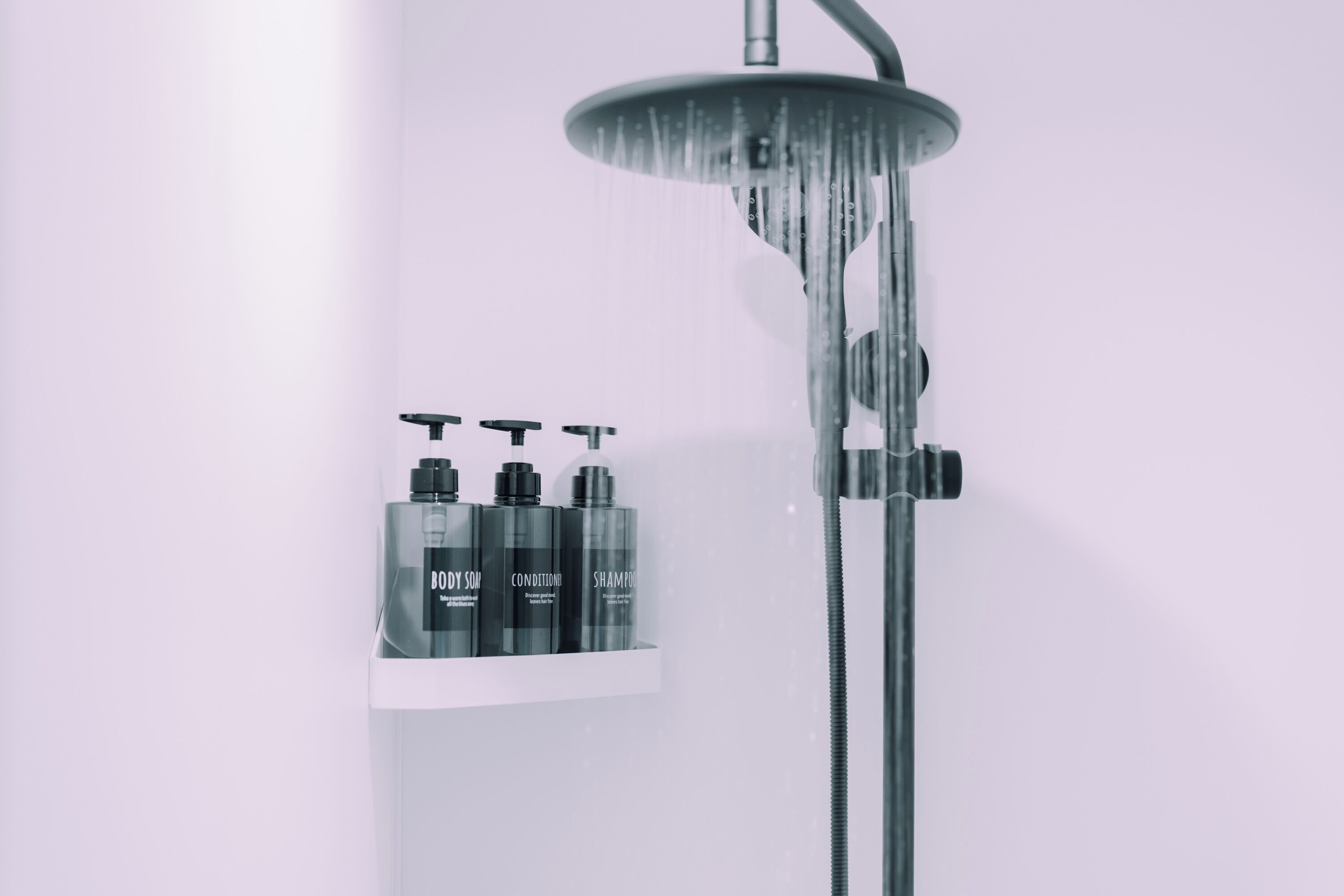 Una ducha moderna con cabezal de ducha de lluvia y un estante con tres productos de cuidado corporal.