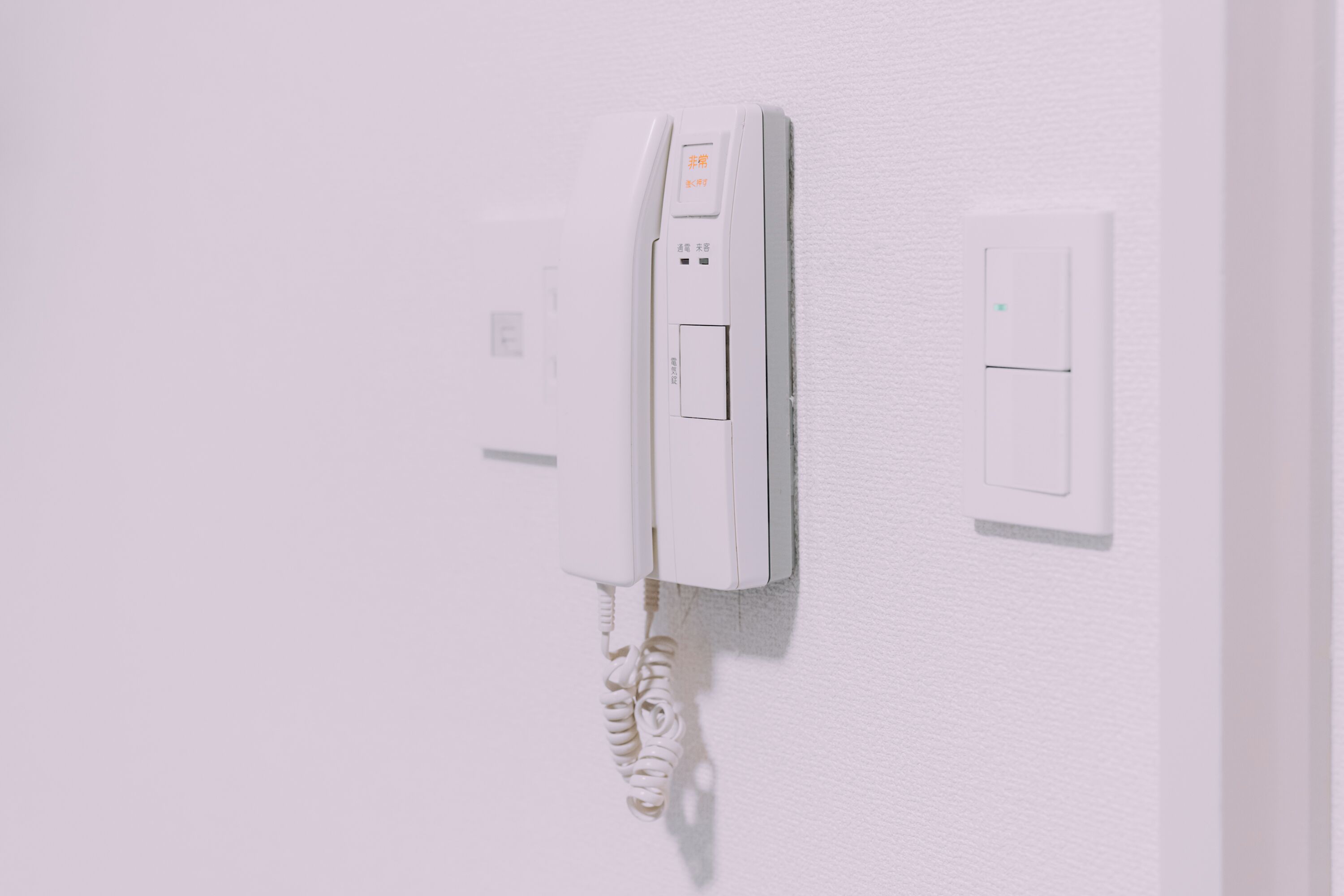 A white wall-mounted telephone with a cord, a power outlet, and a light switch.