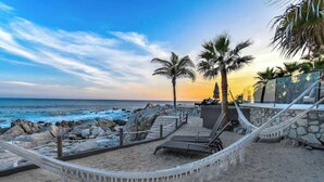 A beachside area with a hammock, lounge chairs, and palm trees.