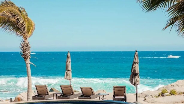 A poolside area with lounge chairs and umbrellas, overlooking the ocean.
