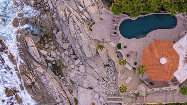 An aerial view of a coastal property with a swimming pool, outdoor seating, and a large circular patio.