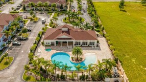A residential area with a large house featuring a swimming pool, surrounded by palm trees and a well-maintained lawn.