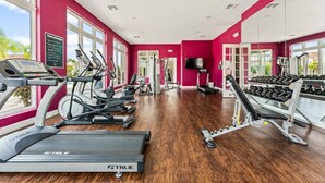 A gym with treadmills, ellipticals, and weight machines, bright pink walls, and large windows.