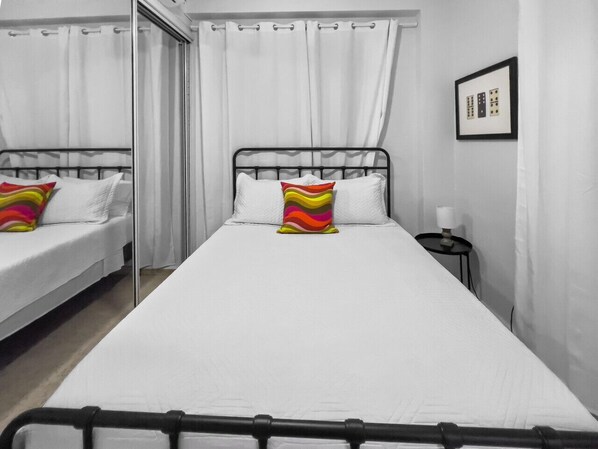 Une chambre avec un lit simple, une table de chevet avec une lampe et un miroir au mur.