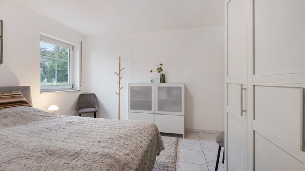 A bedroom with a bed, a chair, a wardrobe, a window, and a lamp.