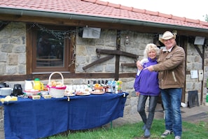 A stone building with a tiled roof, a table with food and drinks, and a person in a brown jacket and cowboy hat. - Holiday Home 'Zum Pferdestall' with Shared Pool, Shared Terrace and Wi-Fi (Dreetz)