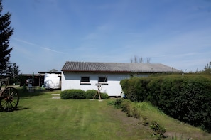 A white house with a sloped roof, a small garden, and a wooden cart. - Holiday Home 'Zum Pferdestall' with Shared Pool, Shared Terrace and Wi-Fi (Dreetz)