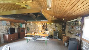 A rustic interior with a wooden ceiling, stone walls, a wooden dining table with benches, a fireplace, and a television on a wooden cabinet. - Holiday Home 'Zum Pferdestall' with Shared Pool, Shared Terrace and Wi-Fi (Dreetz)