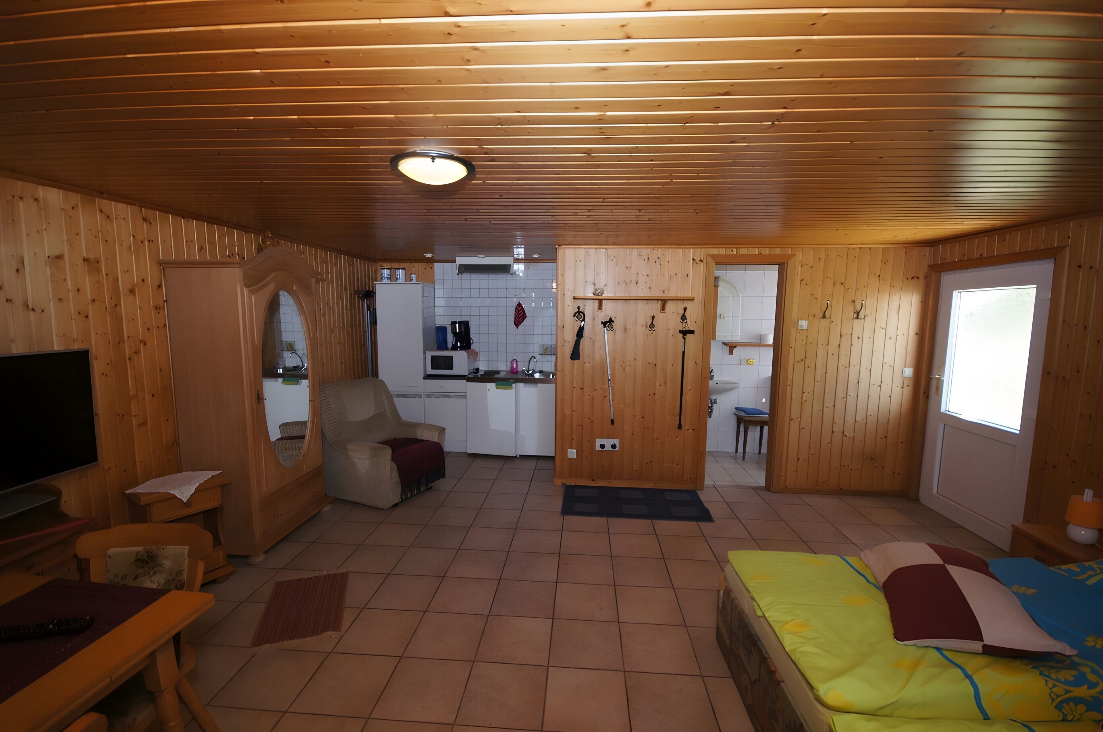 A wooden interior with a TV, sofa, dining table, and a bed.