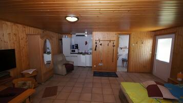 A wooden interior with a TV, sofa, dining table, and a bed.