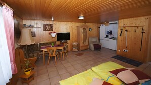 A wooden-paneled room with a dining area, a television, a small kitchen, and a bed with colorful bedding. - Holiday Home 'Zum Pferdestall' with Shared Pool, Shared Terrace and Wi-Fi (Dreetz)