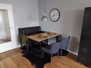 A dining area with a wooden table, two chairs, a clock, and a black cabinet.