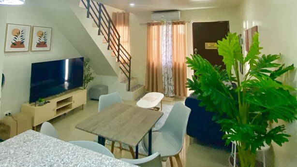 A modern living room with a TV, dining table, chairs, and a staircase.