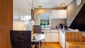 A compact kitchen with a dining area, a window with a view, and a clock on the wall. - Apartment 'Ferienwohnung Klee 2' with Wi-Fi (WHV)