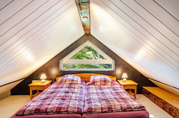 Une chambre à coucher avec un lit, deux tables de chevet, une fenêtre donnant sur des arbres et un plafond en pente.