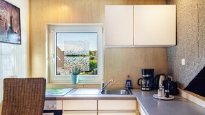 A kitchen with a window, a sink, cabinets, a chair, and a coffee maker. - Apartment 'Ferienwohnung Klee 2' with Wi-Fi (WHV)
