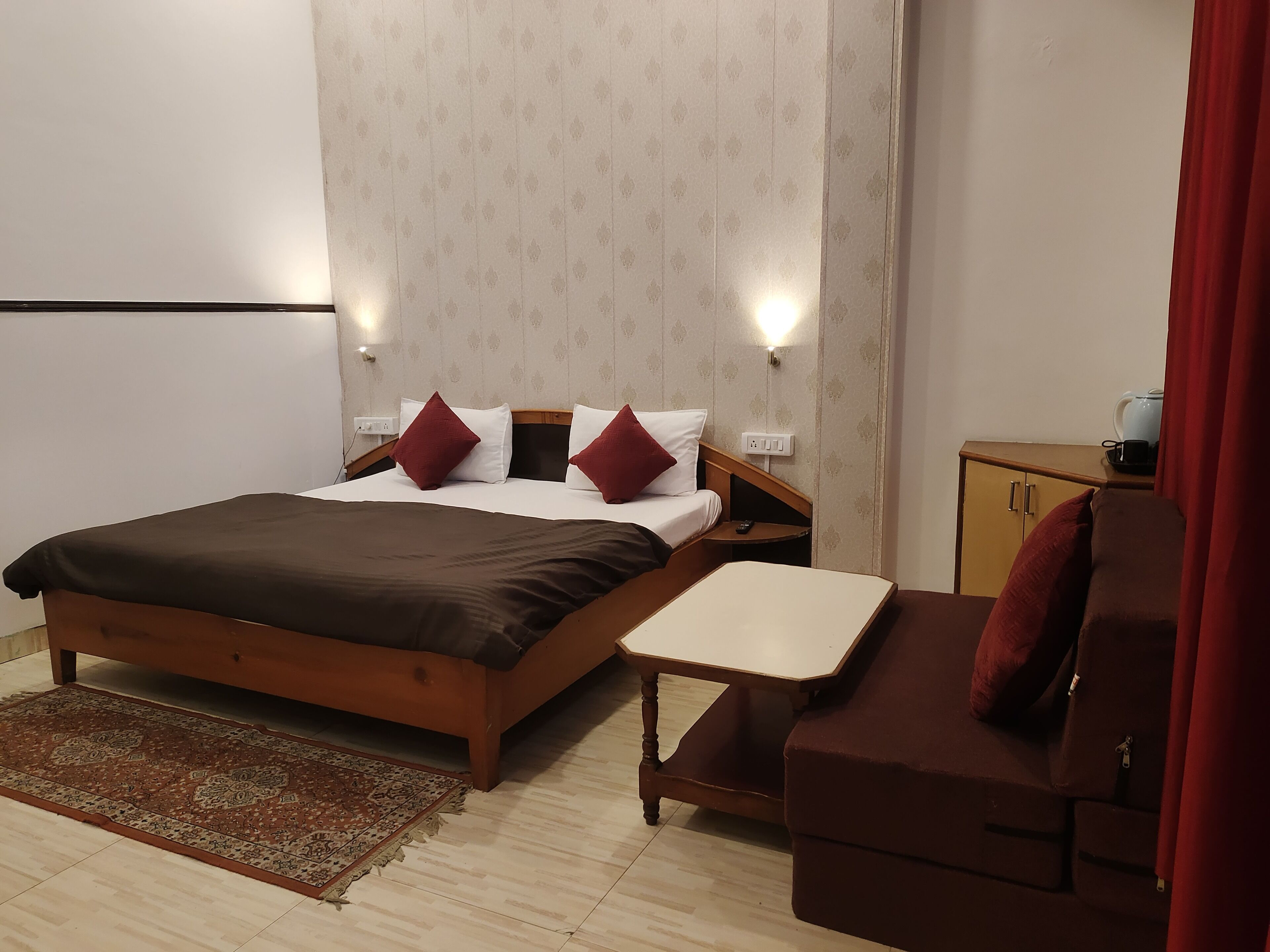 A hotel room with a bed, a small table, a sofa, a carpet, and a wardrobe.