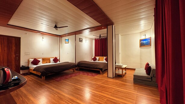 A hotel room with two beds, wooden flooring, ceiling fans, and a small table with a chair. - Plaza Hotel (Pithoragarh)