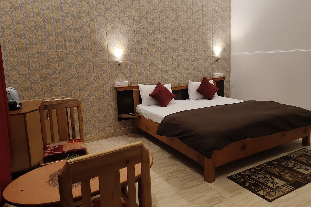 A hotel room with a bed, bedside tables, a chair, a small table, and patterned wallpaper.