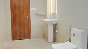 A bathroom with a wooden door, a sink, a toilet, and a mirror. - Plaza Hotel (Pithoragarh)