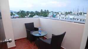 A small balcony with two wicker chairs and a glass table, featuring a clear view of a cityscape with buildings and palm trees. - BLOFT HOTEL (Katpadi)