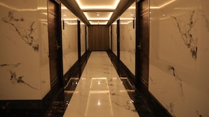 A corridor with marble walls and a polished floor, leading to a room with a curtain. - BLOFT HOTEL (Katpadi)