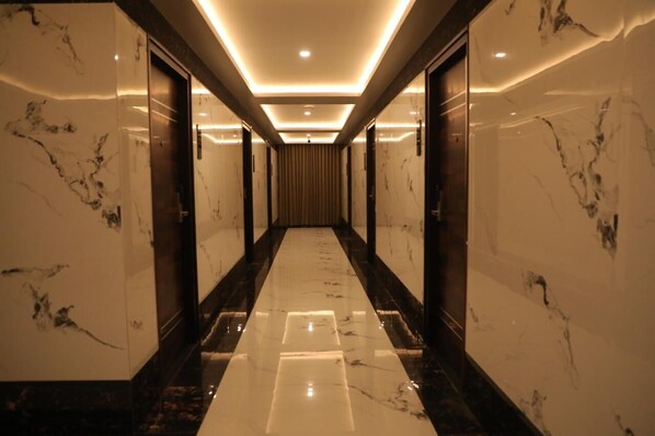 A corridor with marble walls and a polished floor, leading to a room with a curtain. - BLOFT HOTEL (Katpadi)
