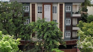 A multi-story building with a modern design, featuring a central vertical panel with a geometric pattern, multiple balconies, and surrounding greenery. - BLOFT HOTEL (Katpadi)