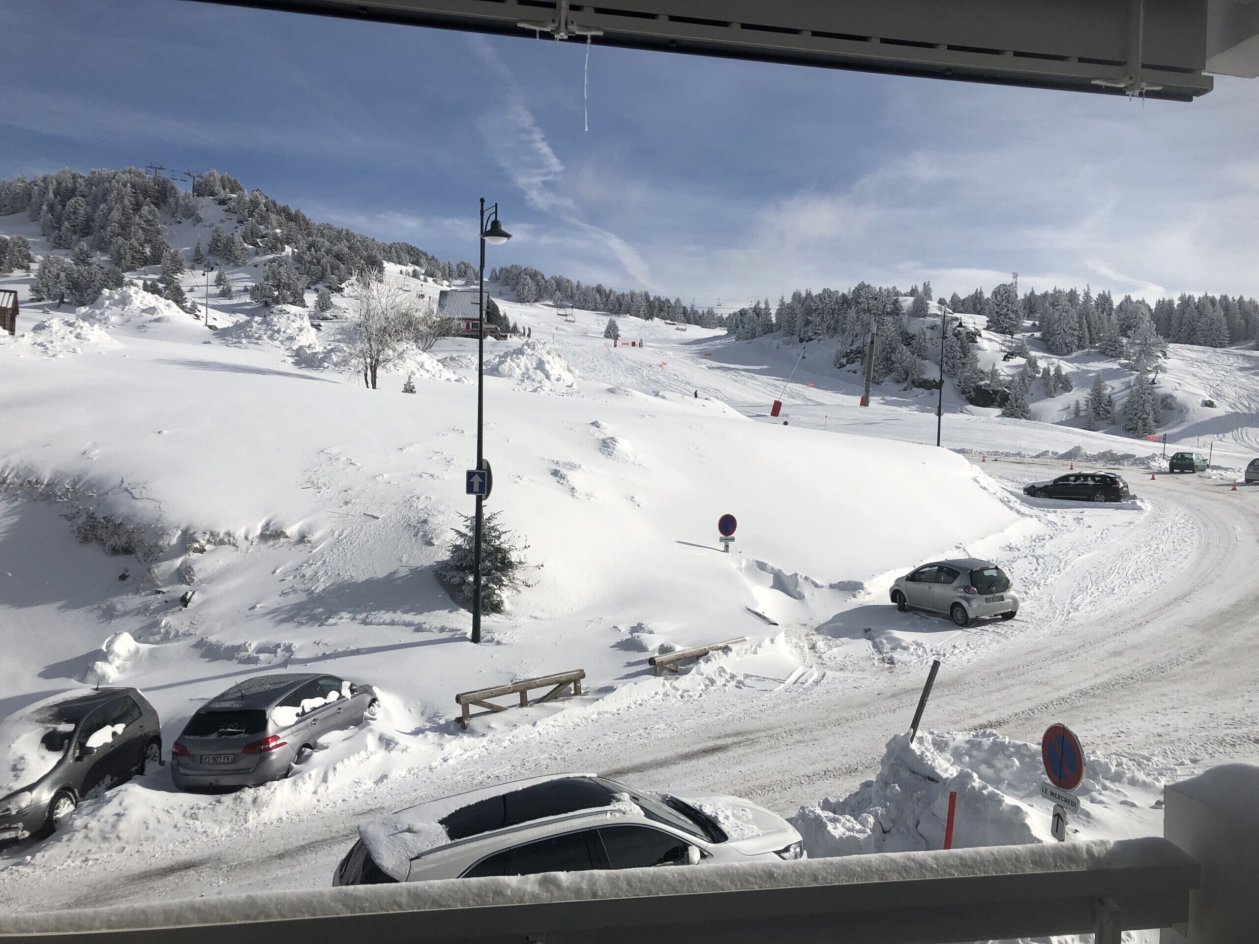 Un estacionamiento nevado, con autos y un telesilla al fondo.