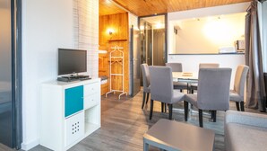 A modern hotel room with a wooden ceiling, a television on a white cabinet, a dining area with grey chairs, and a coat rack. - Bright apt 4/6 ppl, balcony, nears the slopes (Chamrousse)