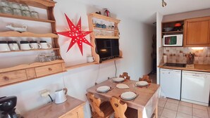 Una cocina compacta con armarios de madera, microondas y una pequeña mesa de comedor con sillas.