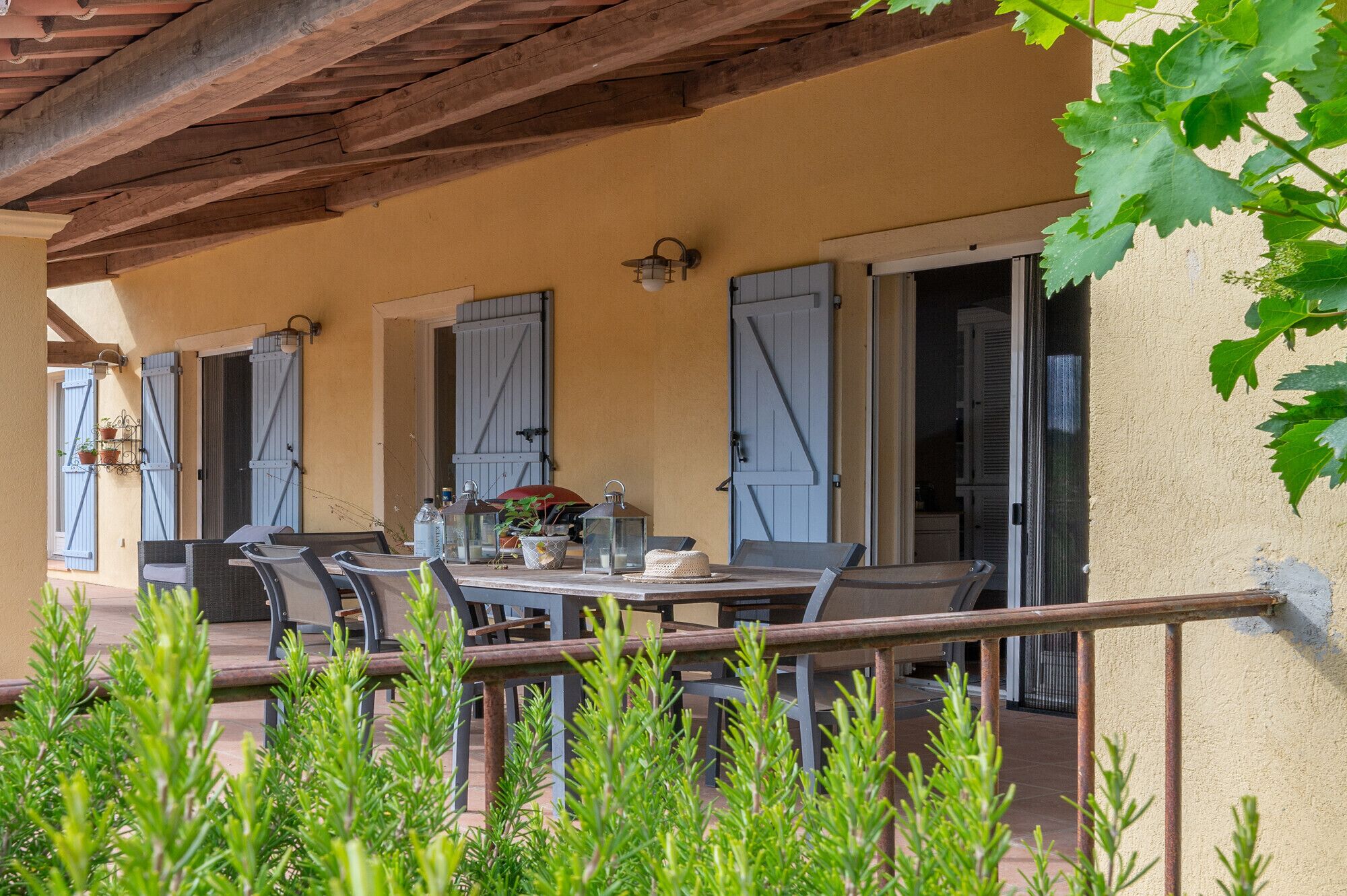 Une terrasse extérieure avec une table et des chaises, une pergola et une vue sur un bâtiment aux volets bleus.