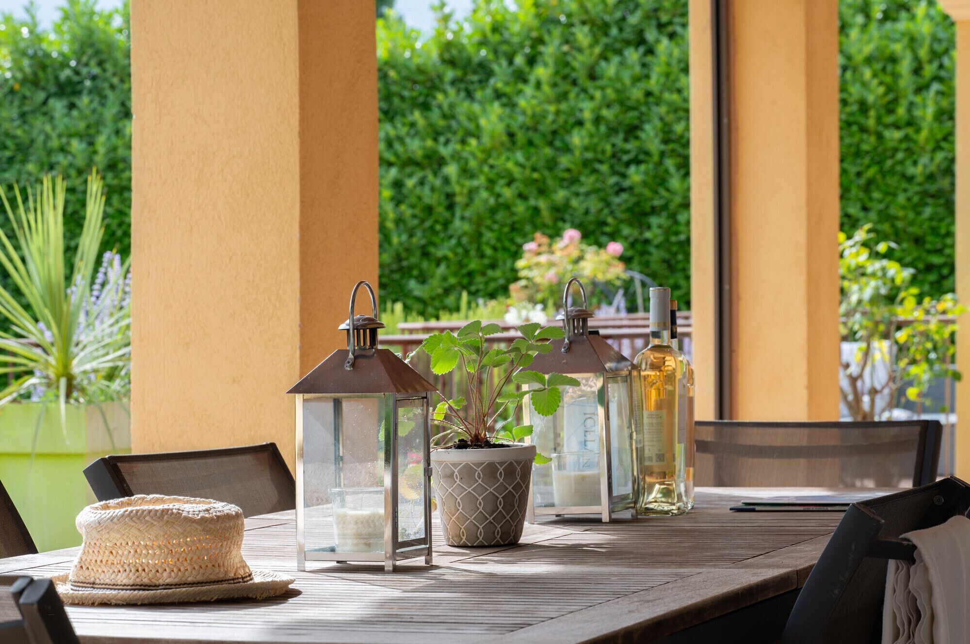 Een houten tafel met een gevlochten mand, een bloempot en twee lantaarns.