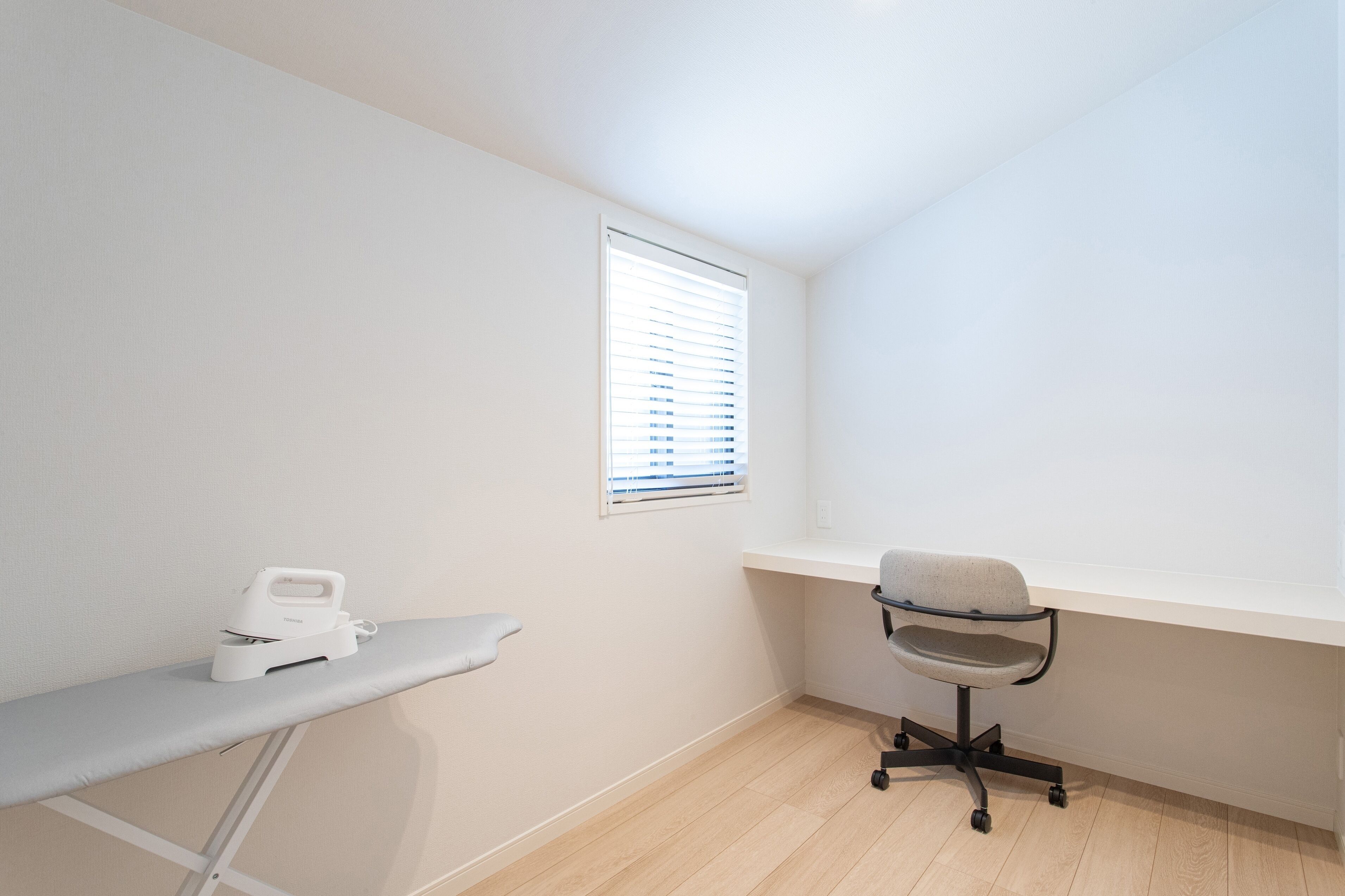 A small, clean room with a white desk, a chair, and a window with blinds.