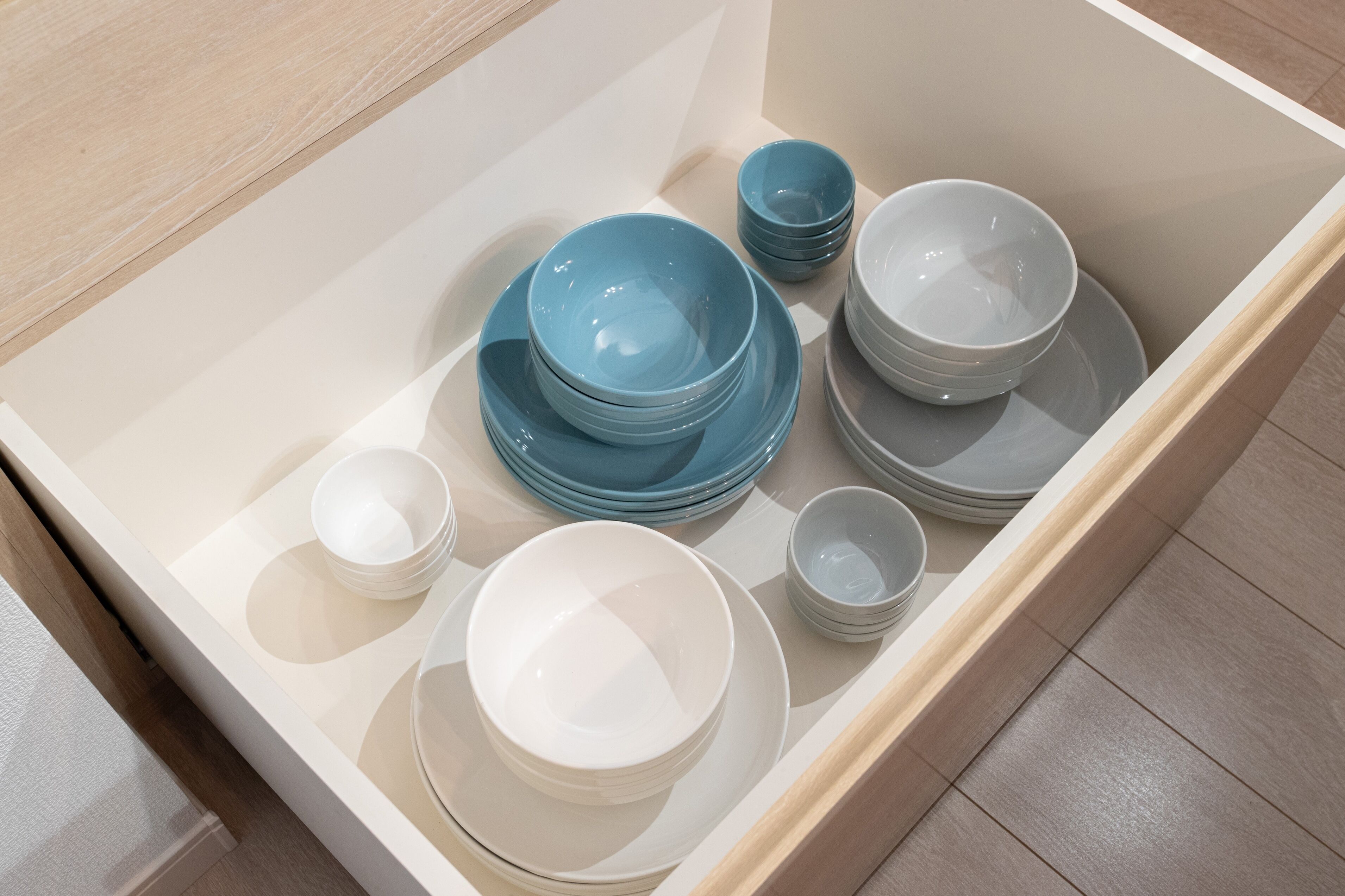 A drawer containing neatly stacked white and blue bowls and plates.